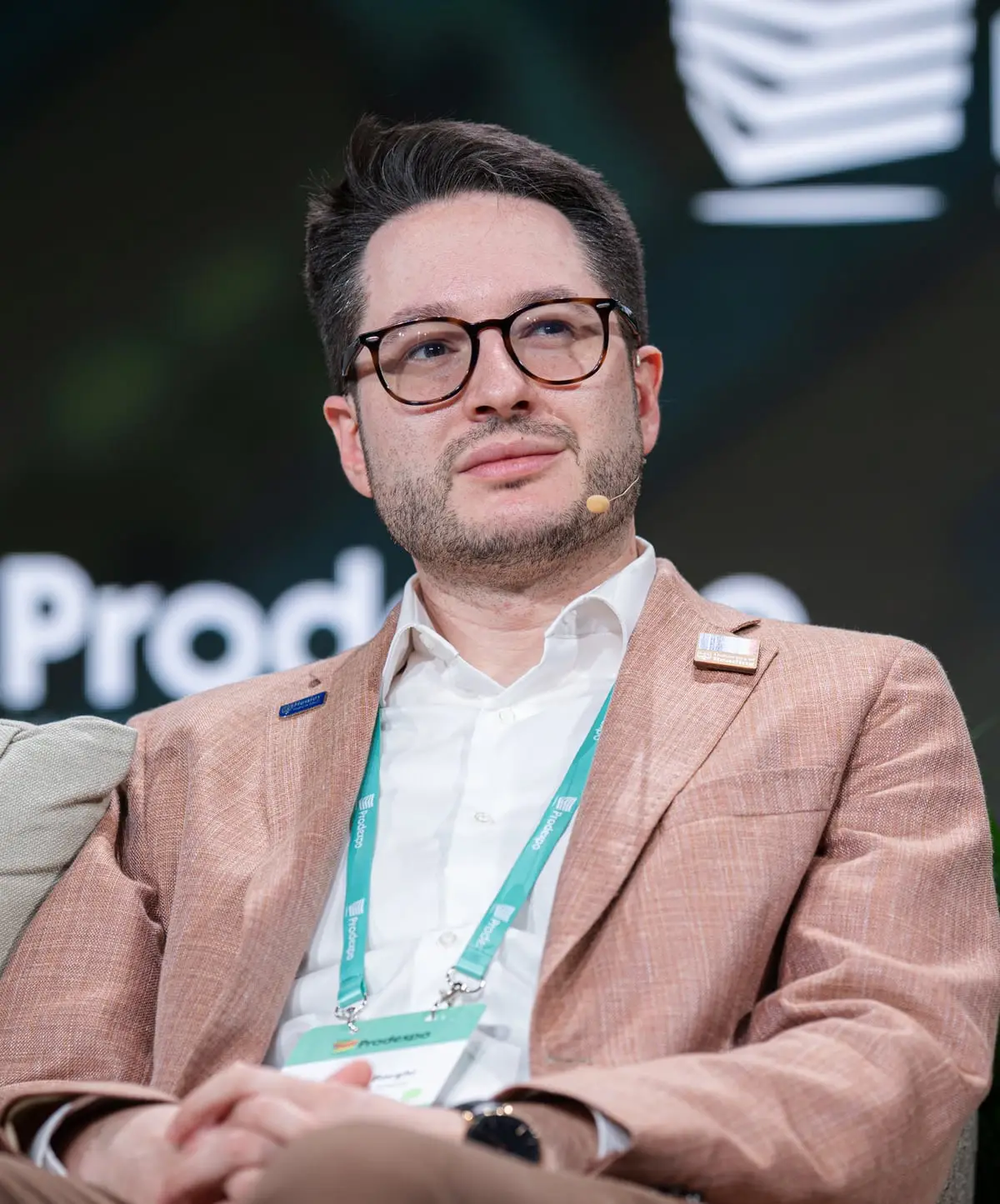 Matteo Borghi, wearing glasses and a terracotta jacket, seated on stage at a conference